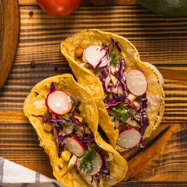 Two Fiesta Mexican tacos filled with chicken, red cabbage, radishes, and cilantro on a wooden board.