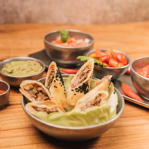 Mexican taquitos with black sesame seeds, guacamole, salsa, and cherry tomatoes on a wooden table.