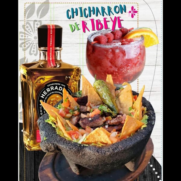 Chicharron de Ribeye in a molcajete with tortilla chips, a Herradura tequila bottle, and a raspberry margarita.