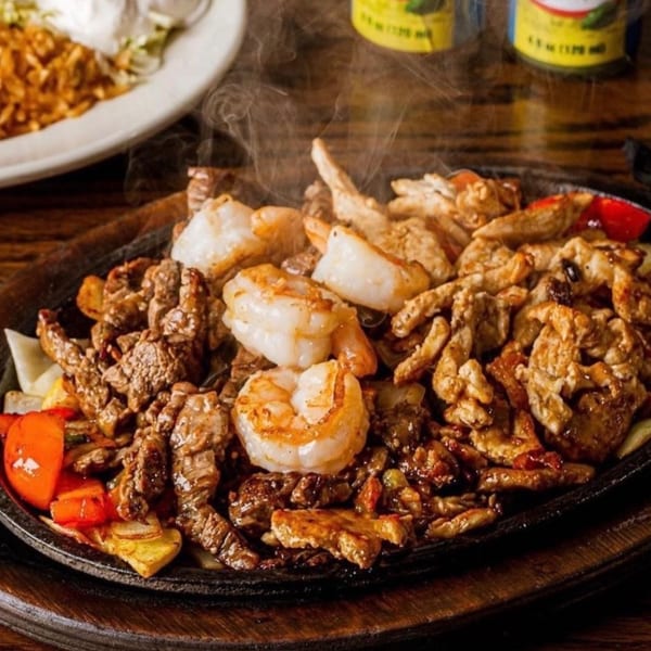 Sizzling Fiesta Mexican fajitas with steak, chicken, shrimp, and vegetables on a hot platter.