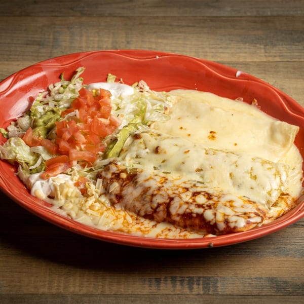 Fiesta Mexican enchiladas with melted cheese, shredded lettuce, diced tomatoes, and guacamole on a red plate.