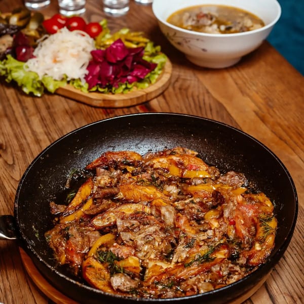 Sizzling fajitas in a black skillet, with a side of pickled vegetables and soup.