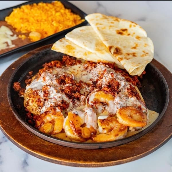 Sizzling Mexican shrimp and chorizo dish with melted cheese, served with tortillas, rice, and beans.