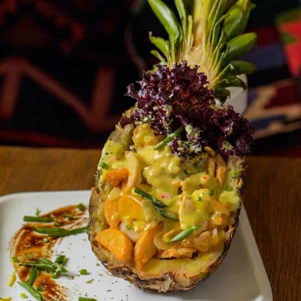 Pineapple filled with yellow saucy chicken, vegetables, and red lettuce, on a white plate.