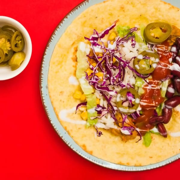 A Mexican burrito on a plate, filled with red cabbage, corn, beans, and jalapeños, with a side of pickled jalapeños.