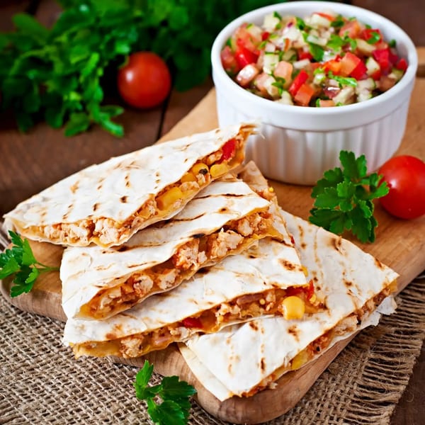Chicken and corn quesadillas with fresh salsa, tomatoes, and parsley on a wooden board.