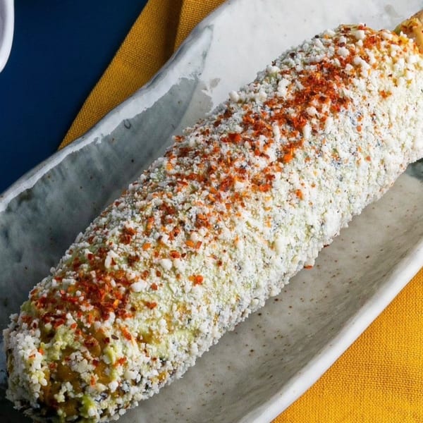 Elote, Mexican street corn, covered in white cheese and red chili flakes on a plate.