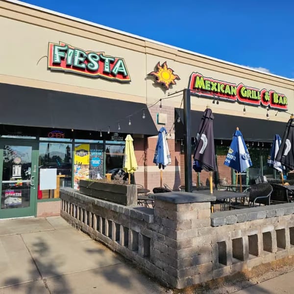 Fiesta Mexican Grill & Bar storefront with outdoor patio seating and umbrellas under a blue sky.